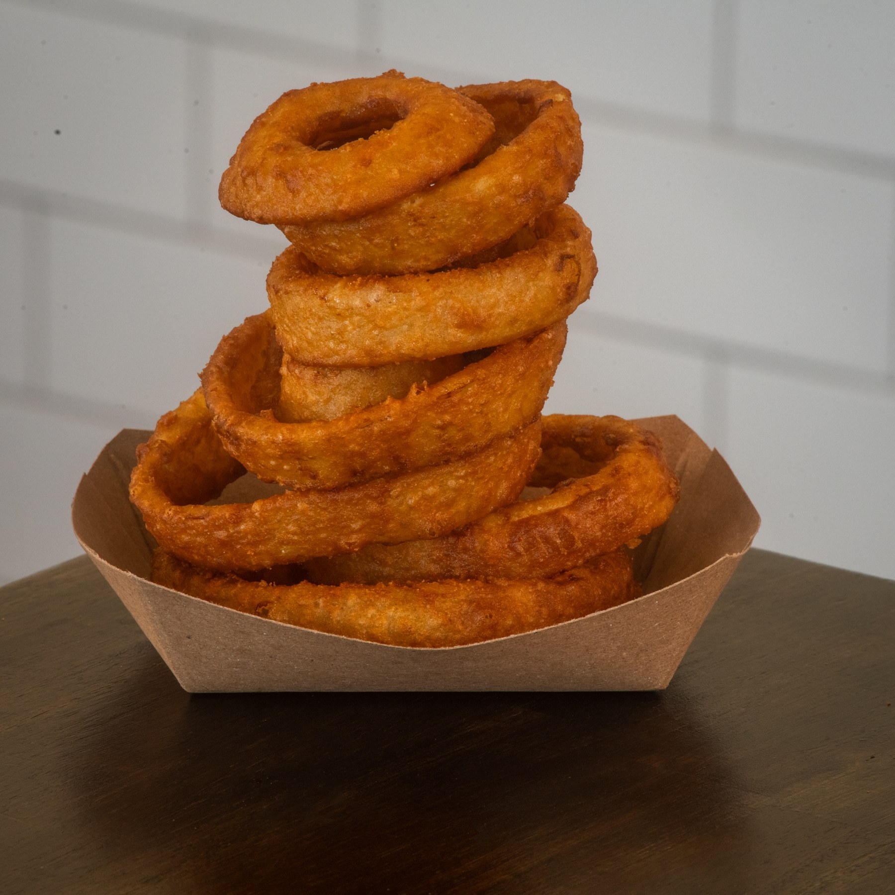 A tall stack of golden onion rings in a paper tray