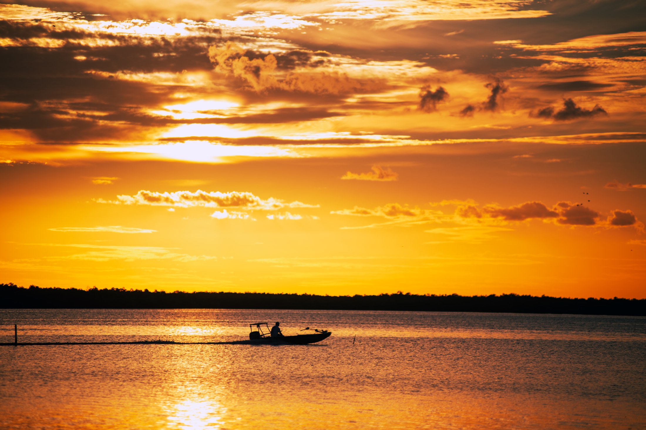 An amber sunset over water with a small boat in silhouette